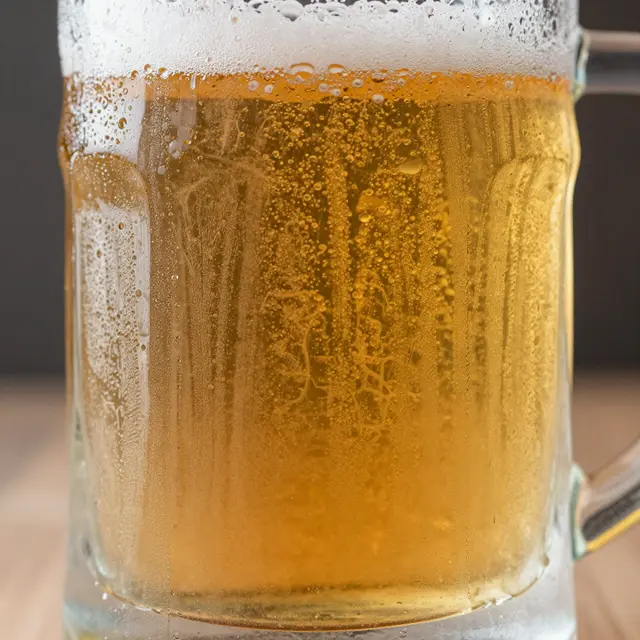 Close up of a frosty glass mug of golden lager covered in condensation and topped with foam