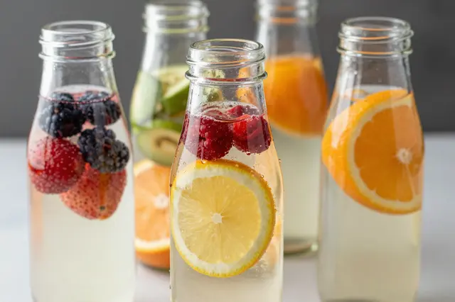 Clear glass bottles hold sparkling infused water with fresh berries and sliced citrus fruit.