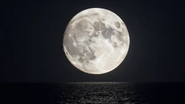 A large detailed full moon hangs above a dark rippled ocean under a deep night sky