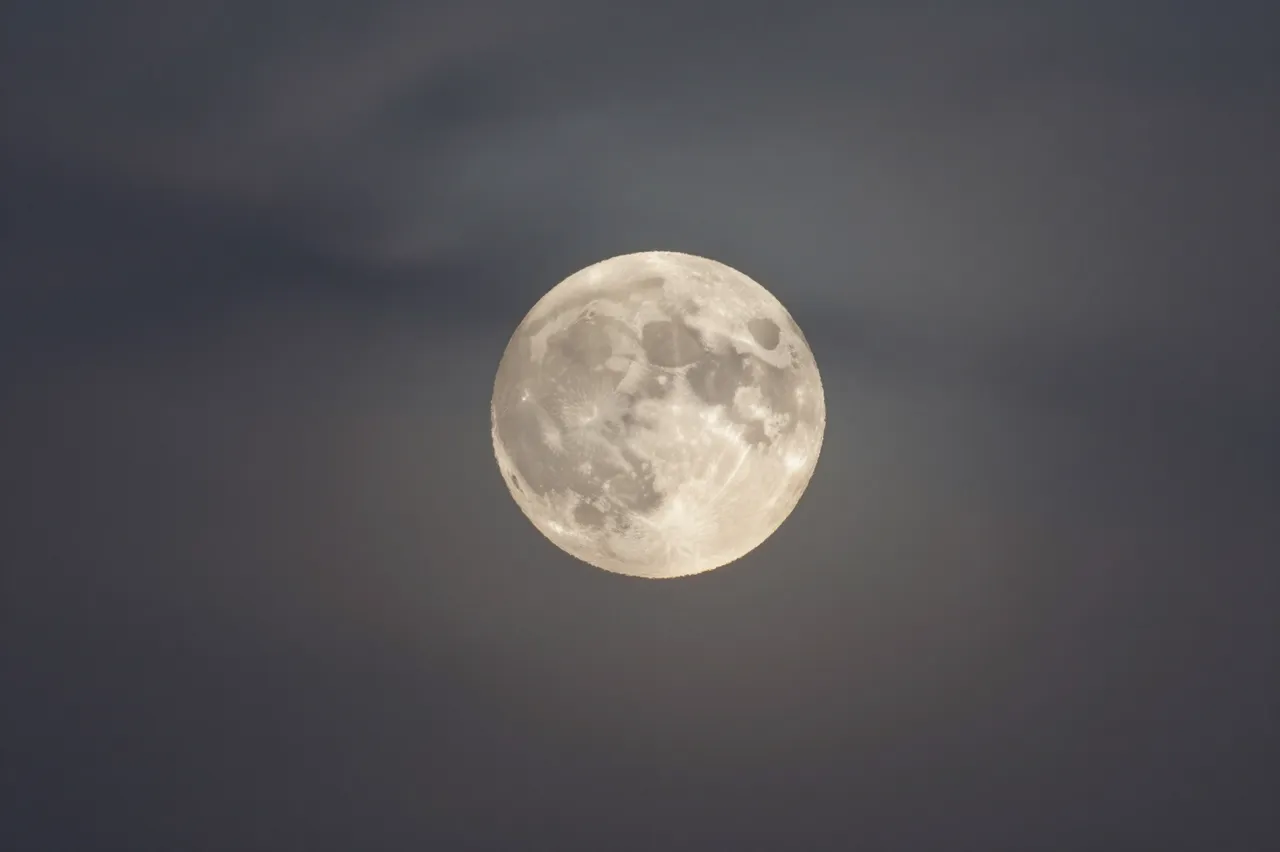 A detailed full moon glows against a dark night sky with faint wispy surrounding clouds