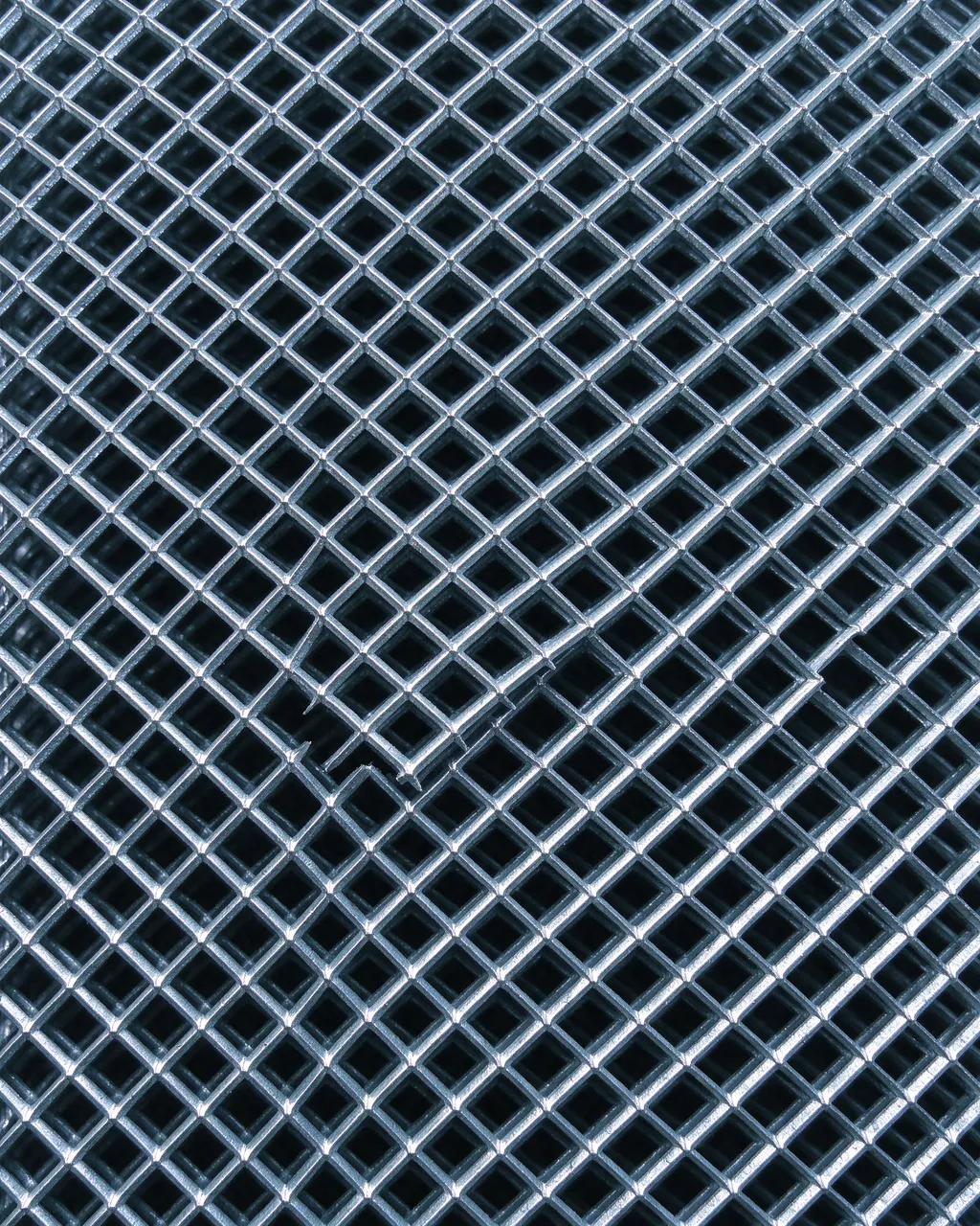 Full frame close-up of galvanized expanded metal mesh with uniform diamond openings against a dark background