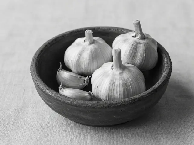Black and white still life of whole garlic bulbs and cloves in a rough clay bowl on linen fabric