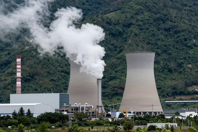 A geothermal power plant releases plumes of steam against a forested mountain backdrop