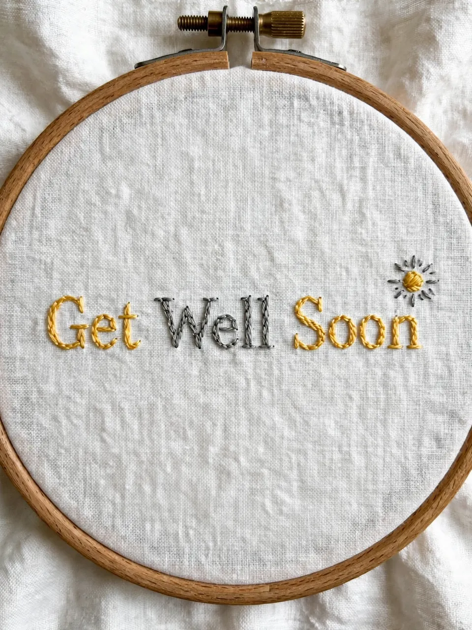 Wooden embroidery hoop with stitched "Get Well Soon" lettering and a small sun on white linen