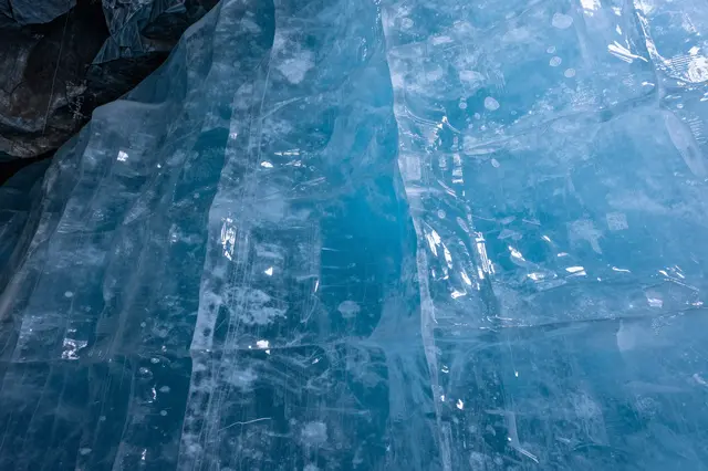Translucent layered blue glacial ice fills the frame inside an ice cave, with dark rock visible at the top left