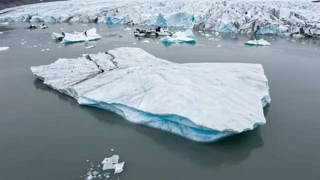 Aerial view of a glacier snout with floating turquoise-tinged icebergs in a gray glacial lake