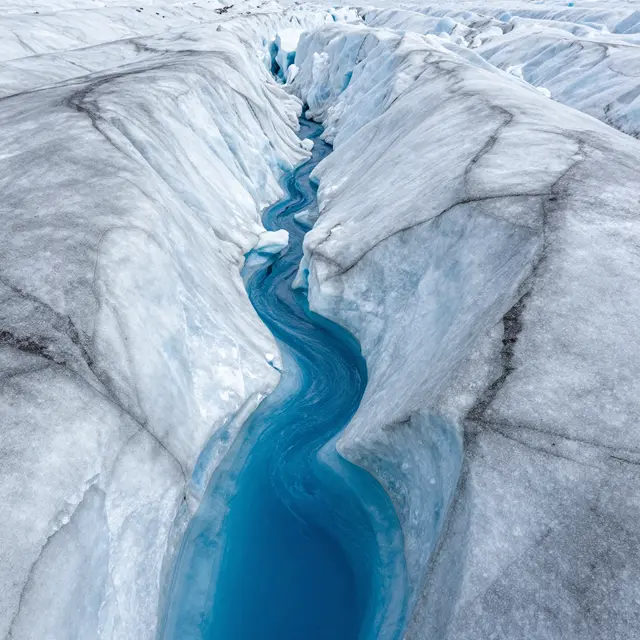 A winding bright blue meltwater stream cuts through textured white glacial ice