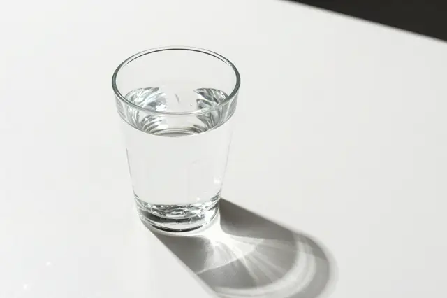 A clear glass of water sits on a white table casting bright caustic light patterns, with empty copy space to the right.