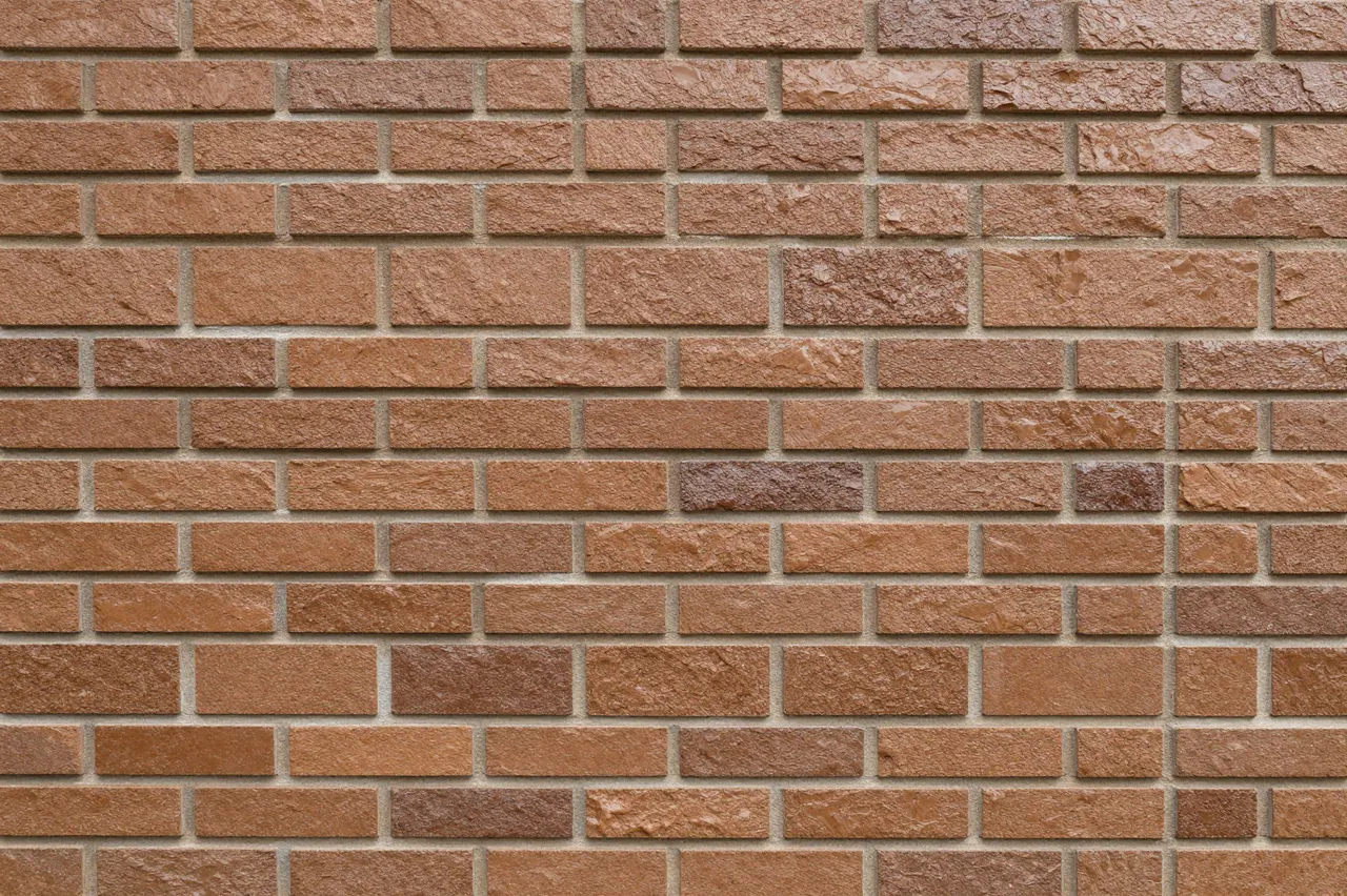 Full frame close-up of a glazed brown clinker brick wall with natural uneven color variation