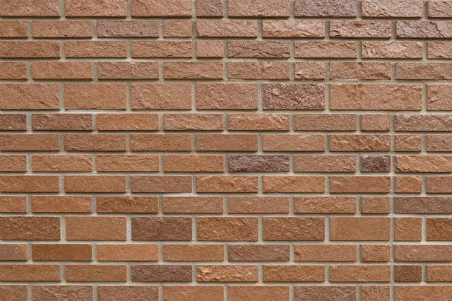 Full frame close-up of a glazed brown clinker brick wall with natural uneven color variation