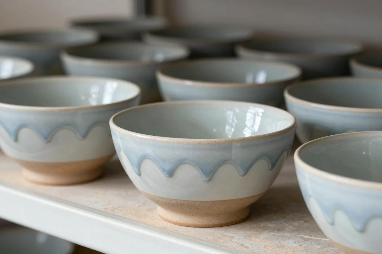 Handmade drippy glaze stoneware bowls cool arranged on a kiln shelf with soft focus background pieces