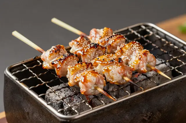 Glazed sesame-topped yakitori skewers rest on a small tabletop charcoal grill.