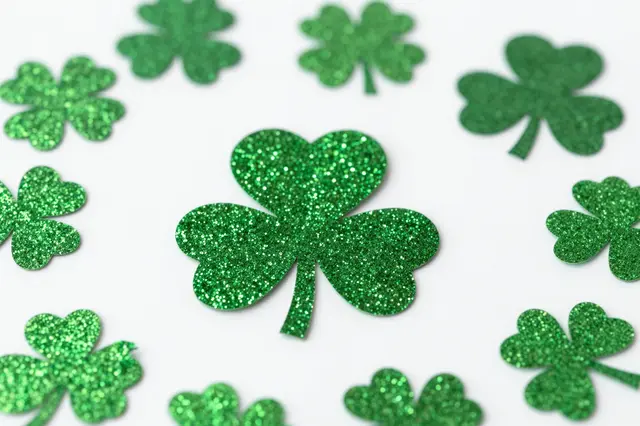 Sparkly green glitter shamrock cutouts arranged on a plain white background with shallow depth of field