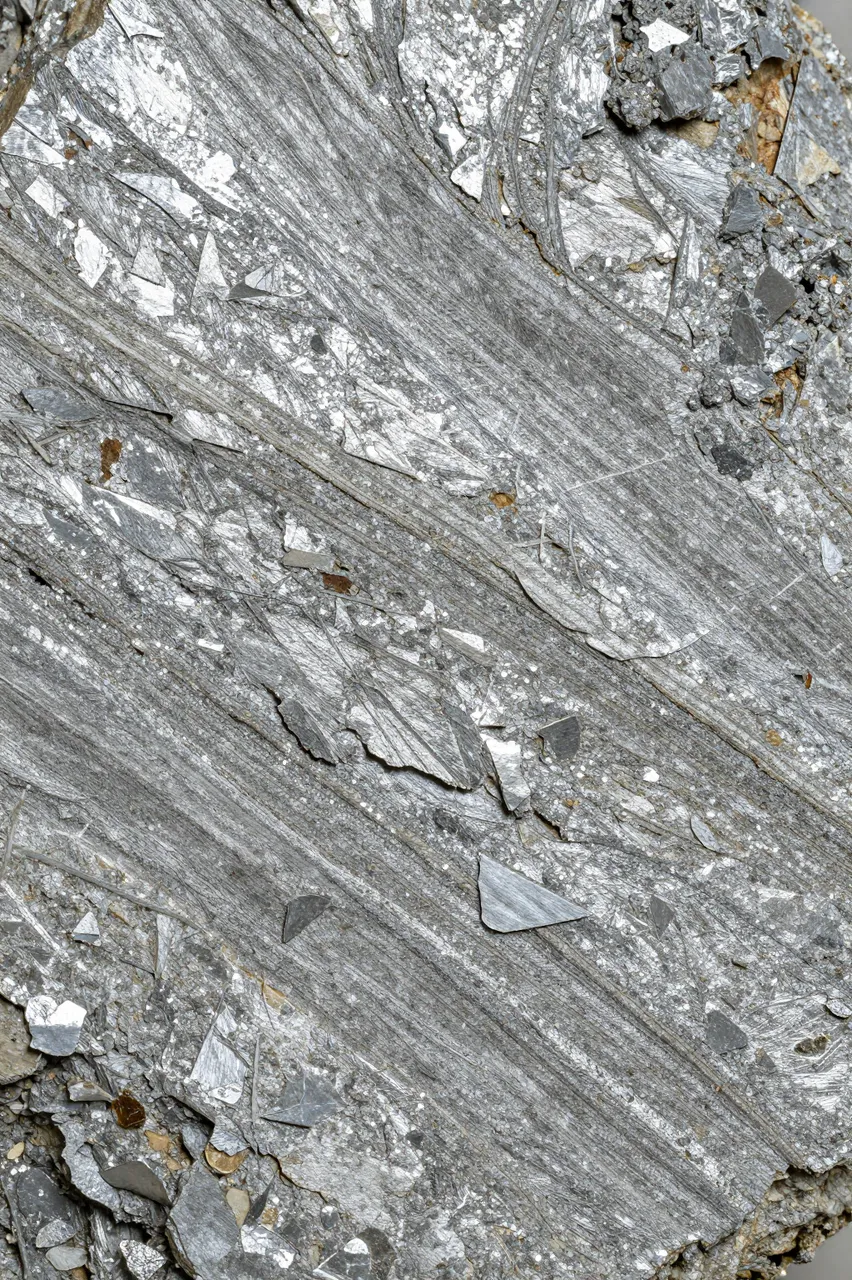 Full frame close-up of silvery flaky mica schist with parallel layered mineral structure