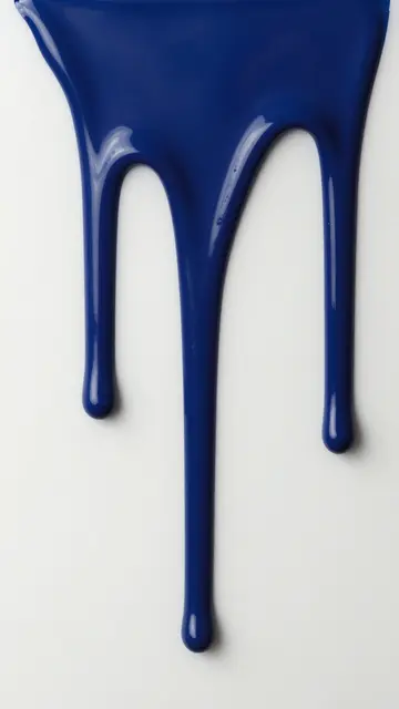 Deep glossy blue enamel paint drips running down a plain white surface