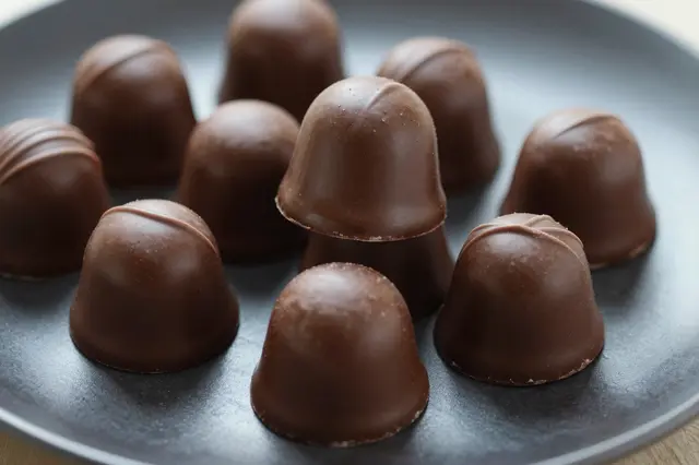 Assorted glossy milk chocolate bonbons arranged on a dark matte plate with soft shallow depth of field.