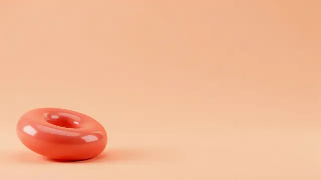 A smooth glossy coral torus rests in the bottom left of a solid peach background with empty copy space