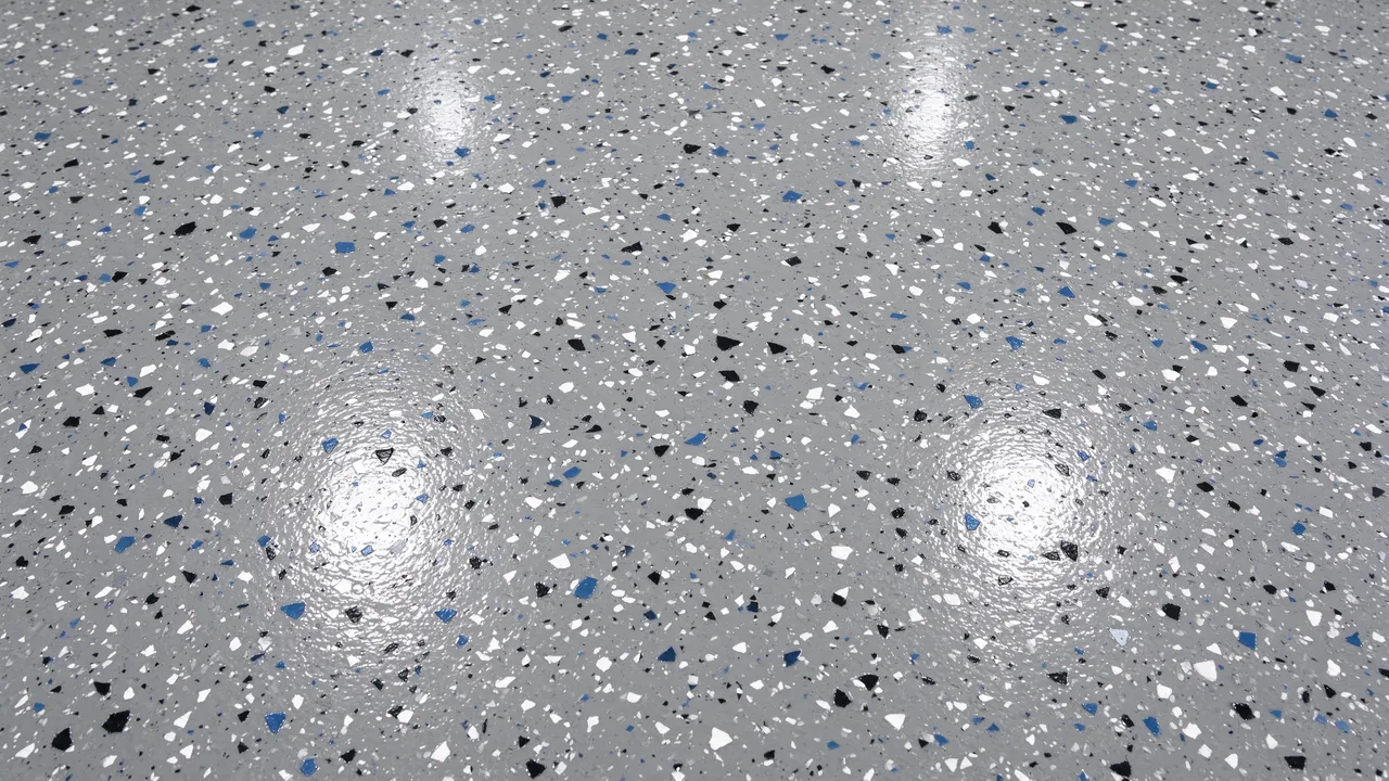 Top view of a glossy gray epoxy floor scattered with black, white, and blue decorative flakes filling the full frame