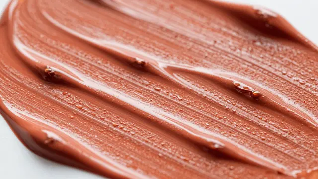 Close-up macro view of raised, glossy wet warm orange acrylic paint strokes on a light background