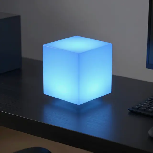 A luminous blue glowing cube hovers above a dark office desk beside a keyboard and monitor edge