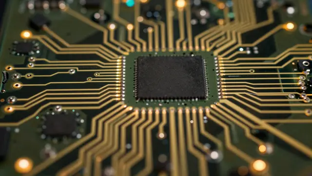Close-up overhead macro view of a circuit board with a central microchip and glowing golden traces
