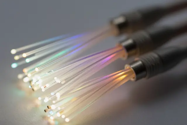 Macro close-up of glowing multicolored fiber optic cable ends resting on a smooth gray surface
