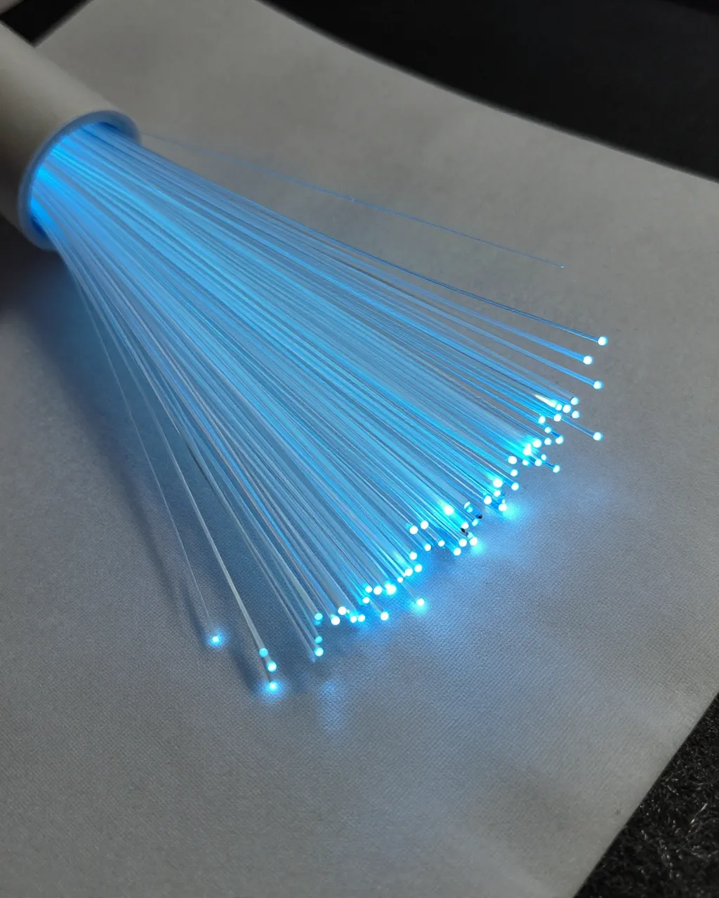 Bright cool blue glowing fiber optic threads rest across a soft white fabric surface