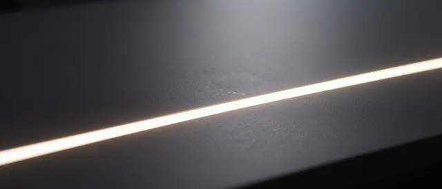 A thin warm glowing light line runs diagonally across a dark textured desk surface with empty copy space above.