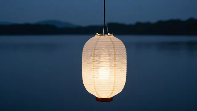 A lit white paper lantern hangs in the foreground above a calm dark lake at blue dusk