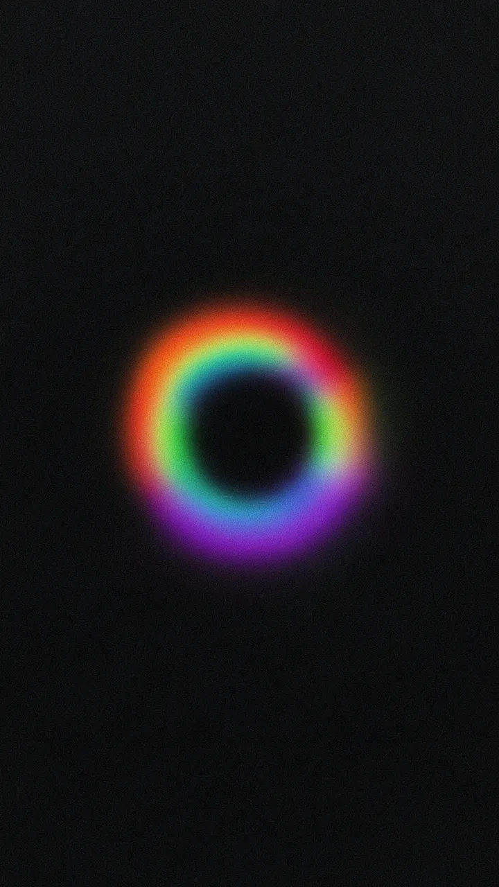 A soft blurry rainbow gradient ring glows against a grainy dark black background
