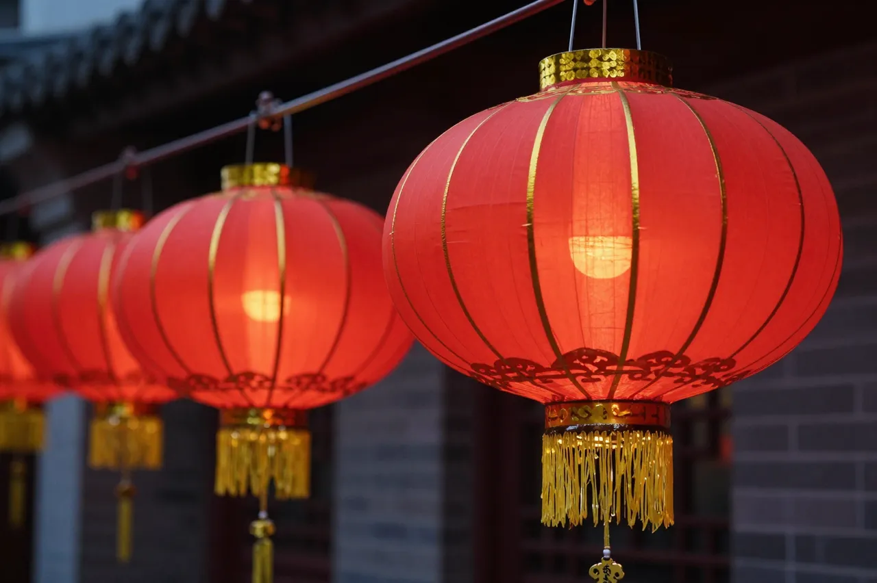 A row of lit red and gold traditional Chinese lanterns hangs in a line outside a building at night.