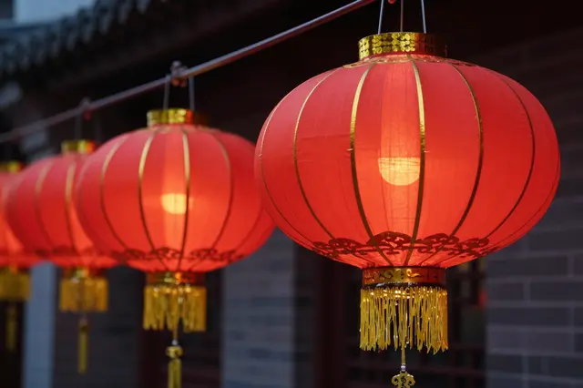 A row of lit red and gold traditional Chinese lanterns hangs in a line outside a building at night.