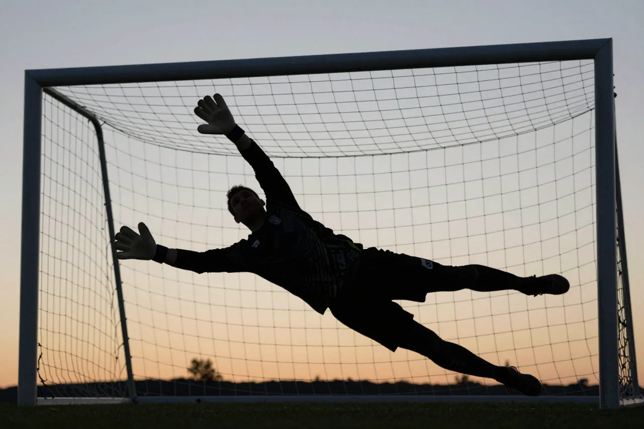 Silhouette of a soccer goalkeeper mid-dive in front of a goal against an evening gradient sky