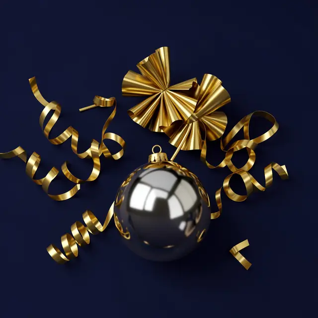 Shiny silver Christmas bauble and curled gold party streamers rest on a deep navy background