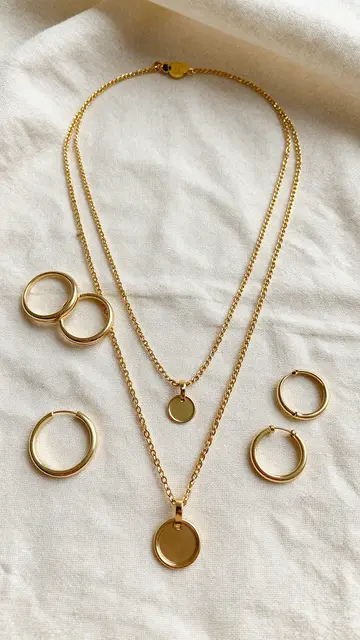 Layered gold necklaces, hoop earrings and stackable rings arranged on crumpled cream linen fabric