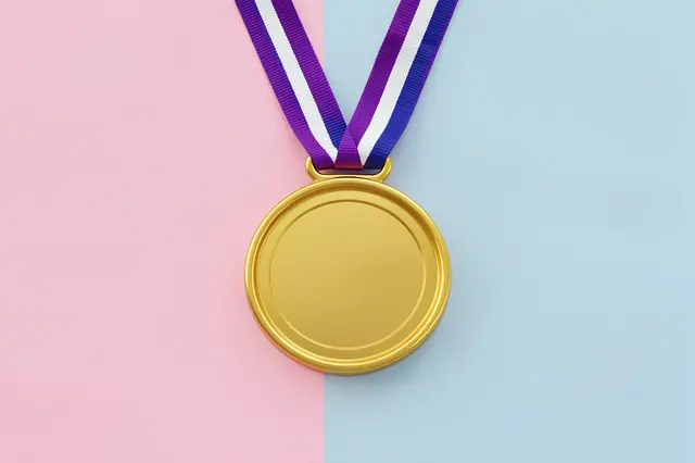 Blank gold medal with a striped ribbon rests on a split pink and light blue pastel background