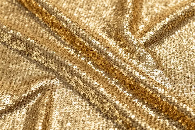 Close-up of draped shimmering gold sequin fabric catching bright reflected light