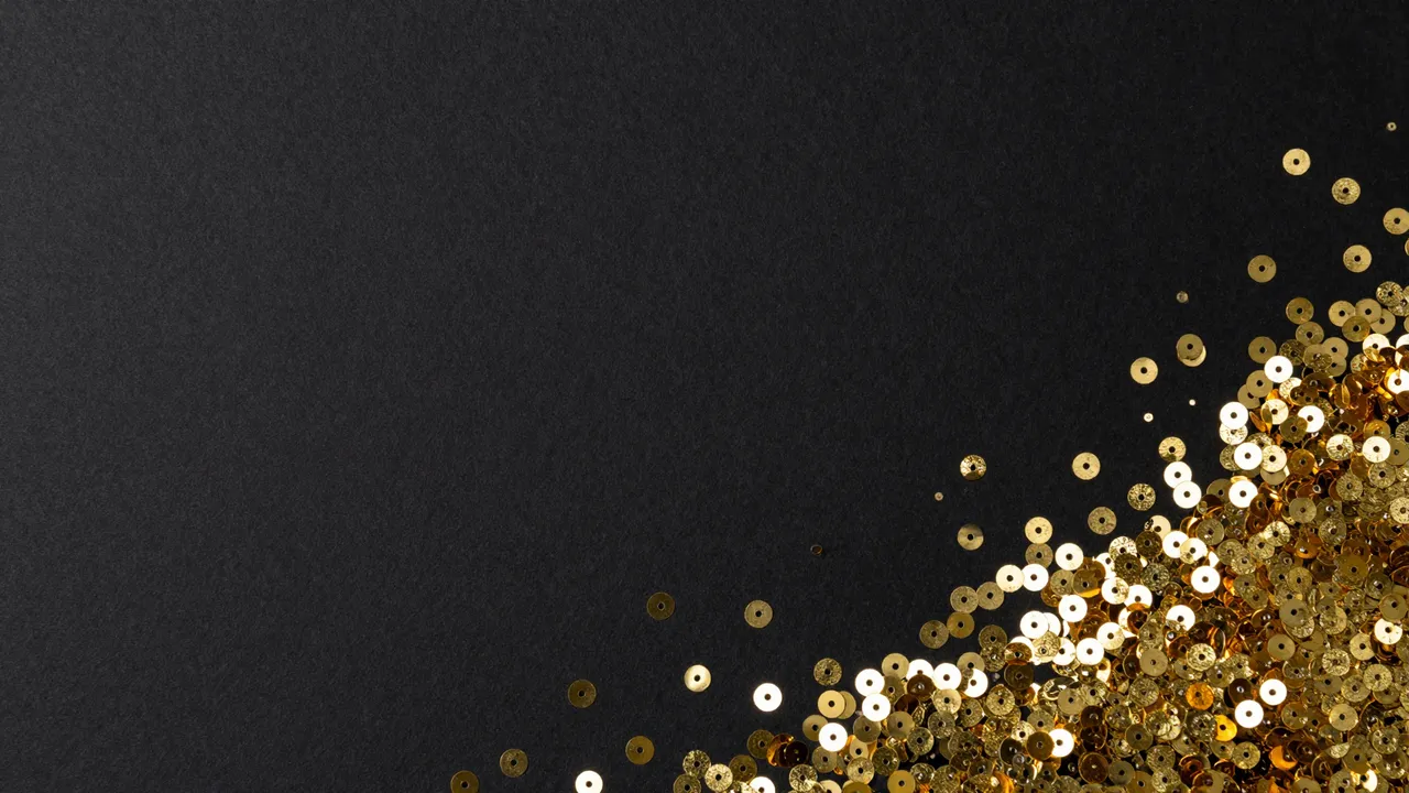 Scattered shiny gold sequins rest in the bottom right corner of a matte black backdrop with empty copy space