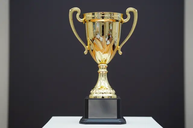 A shiny golden trophy cup rests on a dark base against a plain dark background