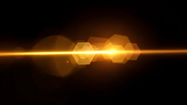 Horizontal warm golden lens flare with soft hexagonal bokeh ghosts on a solid black background