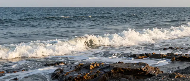 Ocean waves roll onto a dark rocky shore under warm golden hour light