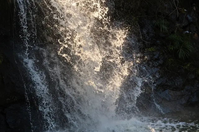 Backlit golden sunlight catches the sparkling spray of a cascading waterfall over dark rocky cliffs.