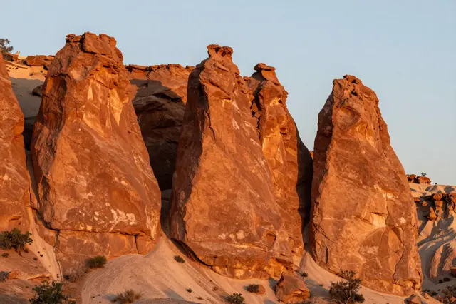 Reddish hoodoo rock spires glow warm orange under soft pale blue early morning sky