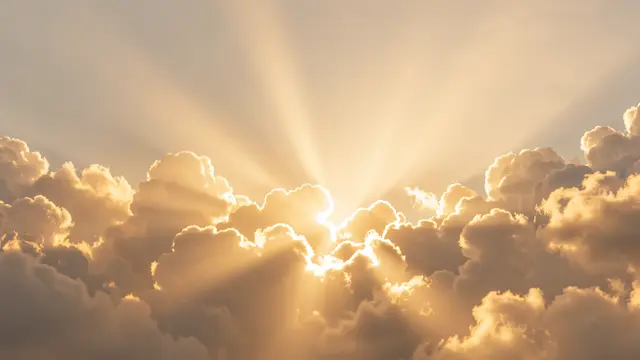Warm golden sunbeams stream past fluffy cumulus clouds with soft empty sky space above.