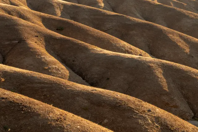 Parallel rolling arid hills catch warm golden sunrise light, casting soft shadows across eroded slopes