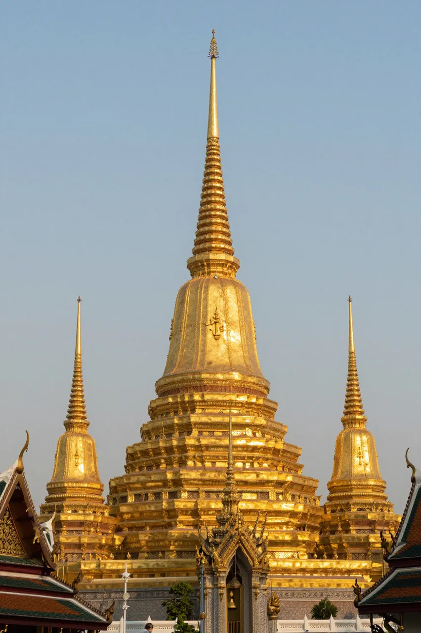 Glowing golden Buddhist temple spires stand against a soft pale sunset sky in Thailand