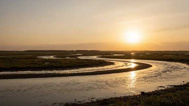 Winding river channels curve through a vast wetland beneath a glowing golden sunset sky