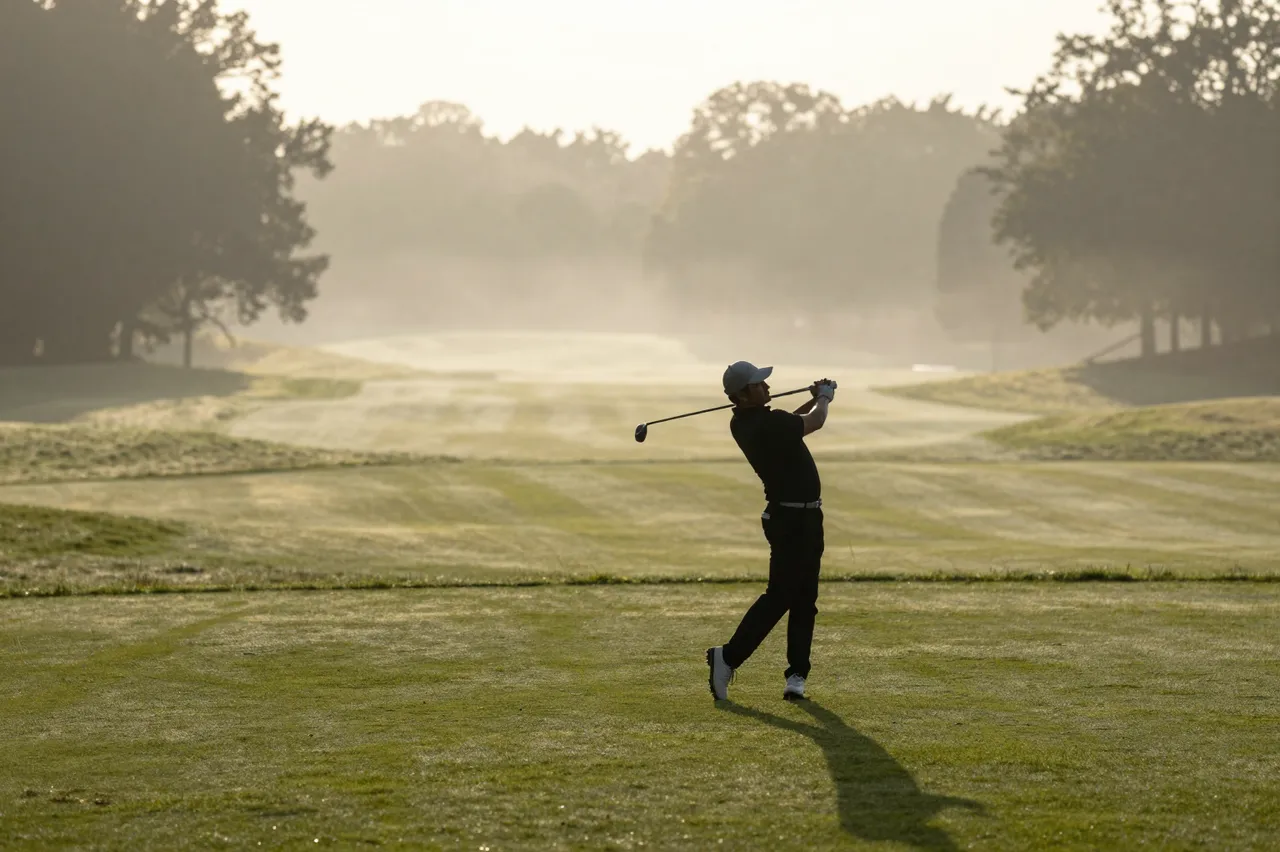 Silhouetted golfer follows through on a swing on a foggy golf course at sunrise