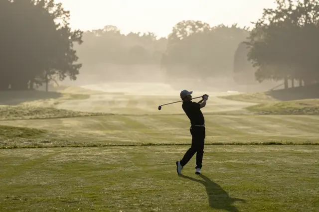 Silhouetted golfer follows through on a swing on a foggy golf course at sunrise