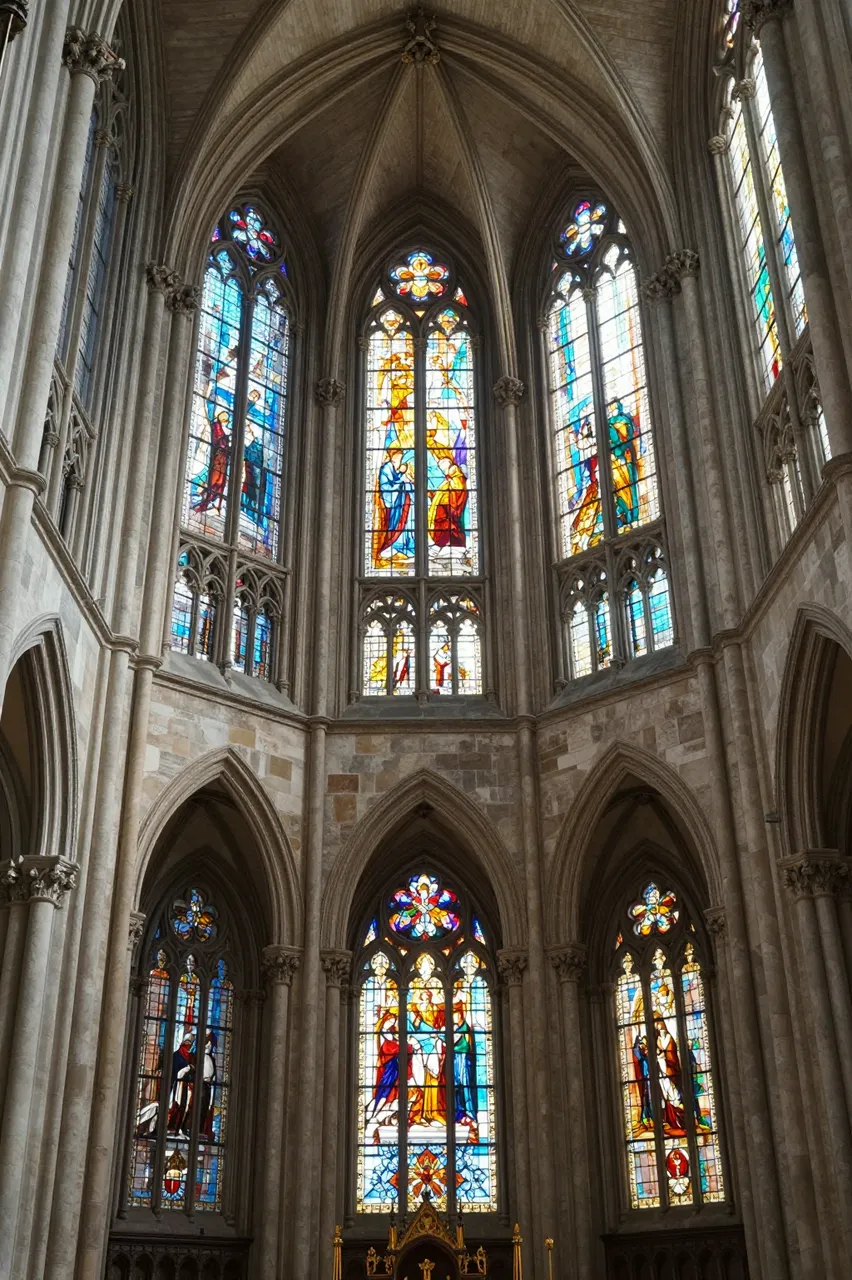 Tall ornate stained glass windows line the stone interior of a gothic cathedral apse